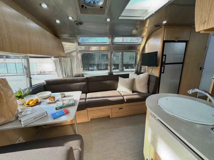 Spacious and modern RV rental interior featuring a living area with sofa, dining table, kitchen, and large windows. Ideal for travel.. Airstream Flying Cloud 2017
