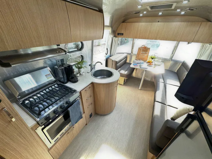 Inside a modern RV rental: a compact kitchen with stove and sink, and a bright dining/living space with wrap-around seating.. Airstream Flying Cloud 2017