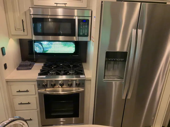 A compact RV rental kitchen featuring modern stainless steel appliances: microwave, range, and a French door refrigerator.. Jayco North Point 2021