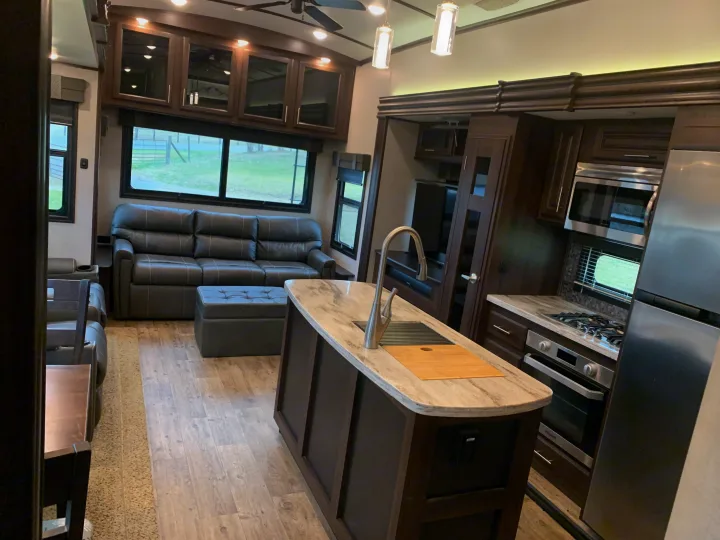 Inside a modern RV rental: a kitchen island, dark leather sofa, and stainless steel kitchen appliances in a spacious layout.. Jayco North Point 2020