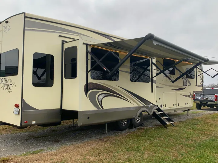 A large, cream-colored Jayco North Point fifth-wheel RV rental with multiple slide-outs and an extended awning.. Jayco North Point 2020