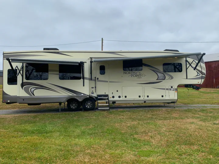 Explore this spacious beige fifth-wheel RV, perfect for your next rv rental adventure, with slide-outs and awnings extended.. Jayco North Point 2020