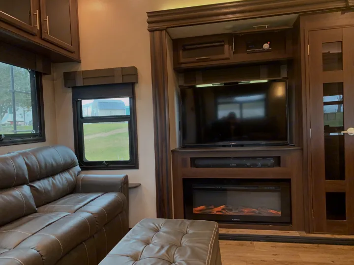 Spacious RV rental living area featuring a plush sofa, entertainment center with TV/fireplace, and scenic window views.. Jayco North Point 2020
