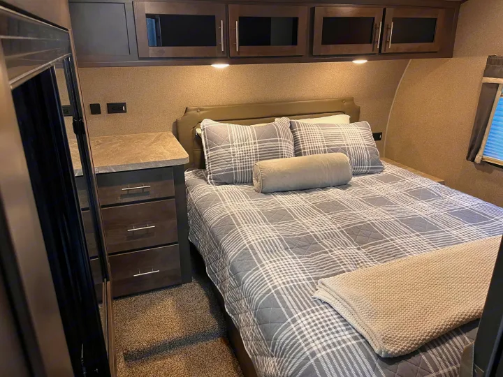 Relax in this cozy RV rental bedroom. Features a comfy bed with plaid bedding, ample storage, and bedside power outlets.. Forest River Rockwood Ultra Lite 2020