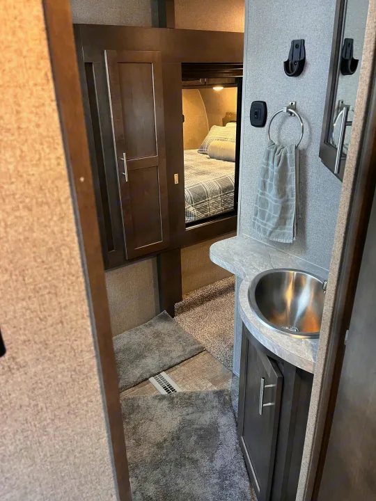Compact RV rental interior featuring a bathroom vanity with a stainless steel sink, leading into a cozy bedroom.. Forest River Rockwood Ultra Lite 2020