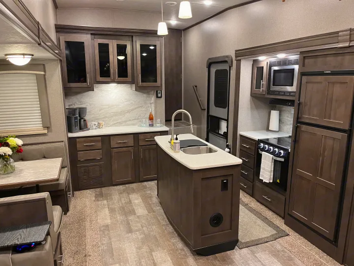 Modern RV rental kitchen and dining area with dark wood cabinets, light countertops, and an island sink.. Forest River Rockwood Ultra Lite 2020