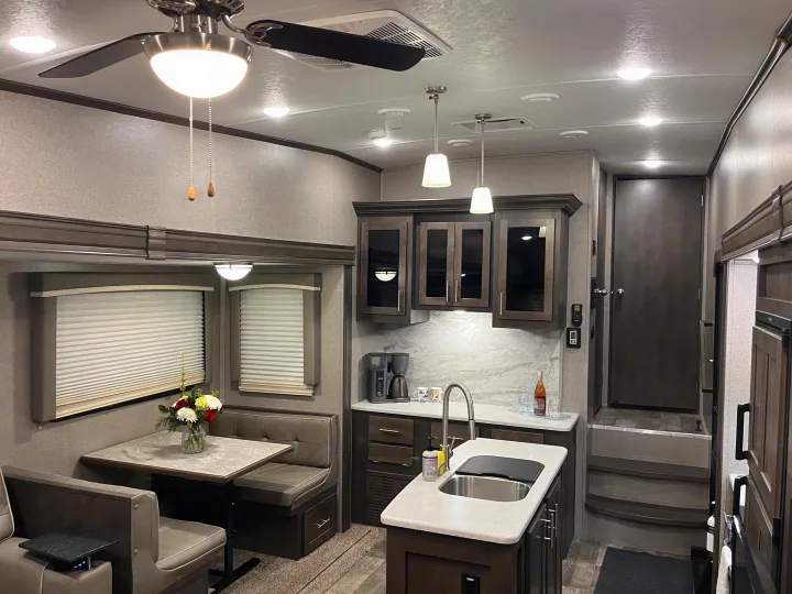 Experience a modern RV rental: comfortable gray dining booth, well-appointed kitchen island with sink, and bright living area with fan.. Forest River Rockwood Ultra Lite 2020