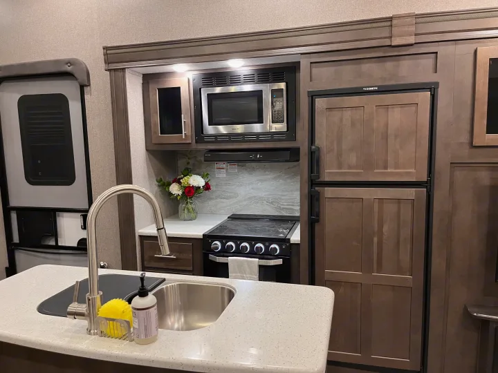 An RV rental kitchen with a stainless steel microwave, oven, sink, and Dometic fridge. Efficient and stylish for travel.. Forest River Rockwood Ultra Lite 2020