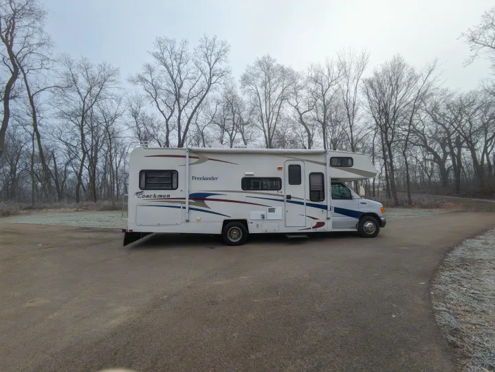 A white Coachmen Freelander RV rental parked on a frosty road amidst bare trees, ready for winter camping.. Coachmen Freelander Deluxe/Premier 2005