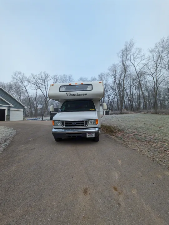 A white Coachmen RV rental with a Wisconsin plate parked on a frosty driveway. Bare trees and house visible. Motorhome.. Coachmen Freelander Deluxe/Premier 2005