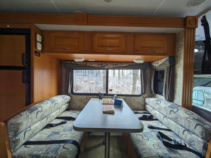 Inside a comfortable RV rental, featuring a dinette with a scenic frosted forest view. Ready for a cozy winter adventure.. Coachmen Freelander Deluxe/Premier 2005