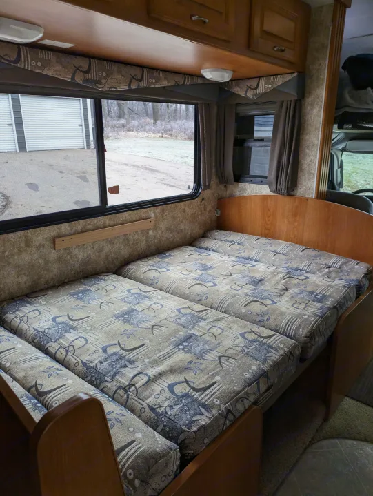 Inside an RV rental: a compact, modular sleeping area with patterned cushions. Window offers a glimpse of a wintery outdoor scene.. Coachmen Freelander Deluxe/Premier 2005