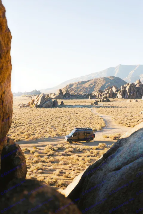 Experience the wild with an RV rental! A black camper van sits on a dirt road amidst rocky desert terrain & mountains.. Mercedes-Benz Sprinter 2021