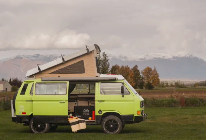 A bright green pop-top VW camper van, ideal for RV rental, is parked in a grassy field with snowy mountains in the background.. Volkswagen Westfalia 1984