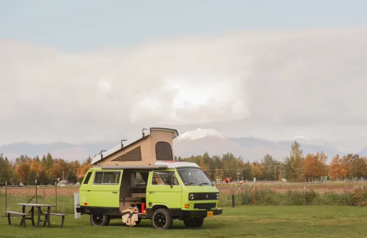 Green pop-top VW van parked in a grassy field with a picnic table, mountains, and autumn trees. Perfect for your next rv rental adventure.. Volkswagen Westfalia 1984