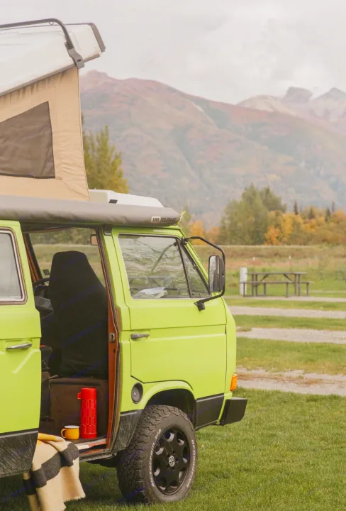 Vibrant green VW camper van with pop-top, parked in a scenic autumn mountain campsite. Perfect RV rental for adventure.. Volkswagen Westfalia 1984