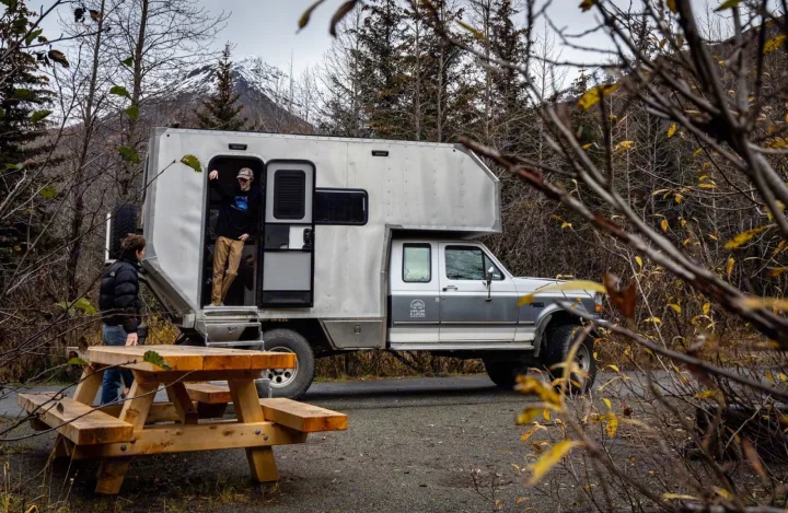 Adventure awaits with this unique rv rental! Two people near their robust camper with mountain views and a picnic table.. Ford F250 1997