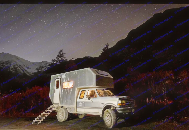 A truck camper RV rental glows under a starry night sky, parked in the mountains. Ideal for remote adventures.. Ford F250 1997