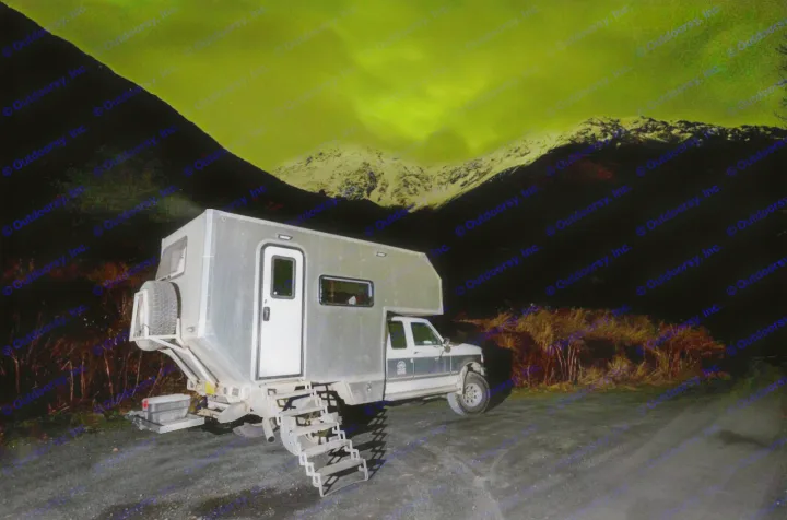 Experience the Aurora Borealis in an RV rental! A camper truck parked at night, mountains glowing green.. Ford F250 1997