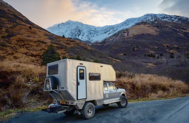 Rugged camper truck, ideal for an RV rental adventure, parked on a mountain road with snow-capped peaks.. Ford F250 1997