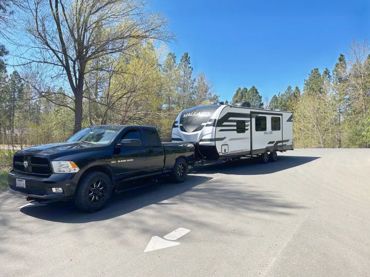 Black Ram 1500 pickup truck towing a white Mallard travel trailer on asphalt. Explore RV rental for your next outdoor trip.. Heartland RVs Mallard 2021