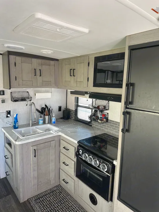This RV rental kitchen features a double sink, modern cabinets, stove, microwave, and fridge, offering practical comfort.. Heartland RVs Mallard 2021