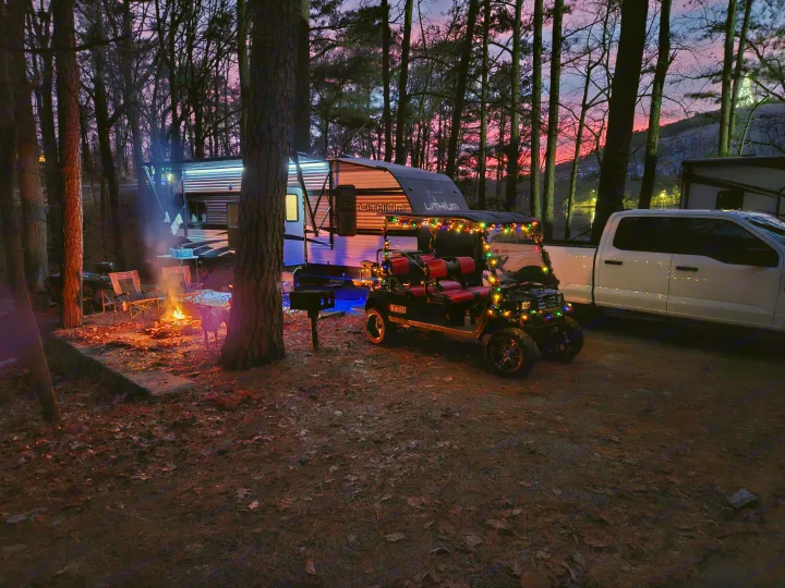 Cozy RV rental campsite at sunset with a glowing campfire, decorated golf cart, and truck under a vibrant sky. Perfect for outdoor adventures.. Heartland Lithium 2021