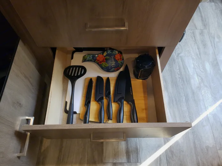 An open, organized kitchen drawer in an RV rental, holding essential knives, a spatula, and a floral spoon rest.. Grand Design Imagine XLS 2022