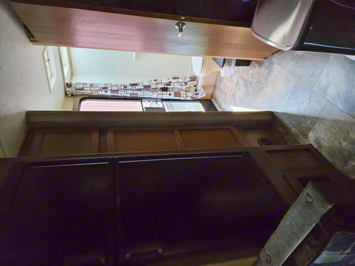 Inside an rv rental: View into a compact RV bathroom with a toilet, patterned shower curtain, and tiled floor.. Coachmen Apex 50th Anniversary 2015