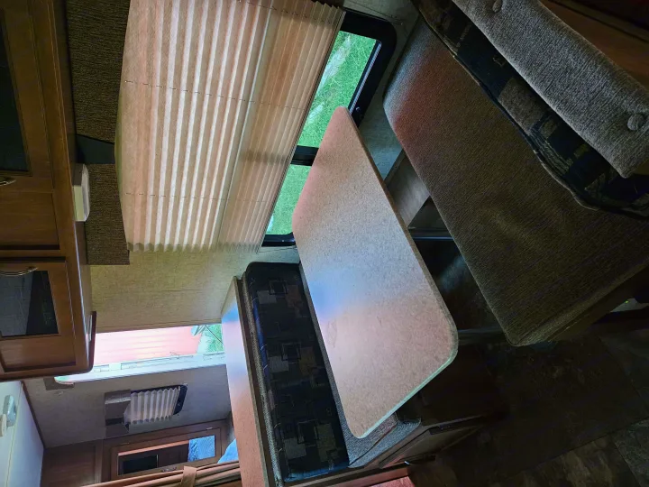 Inside an RV rental: a cozy dinette area with table, upholstered benches, and a window for scenic views.. Coachmen Apex 50th Anniversary 2015