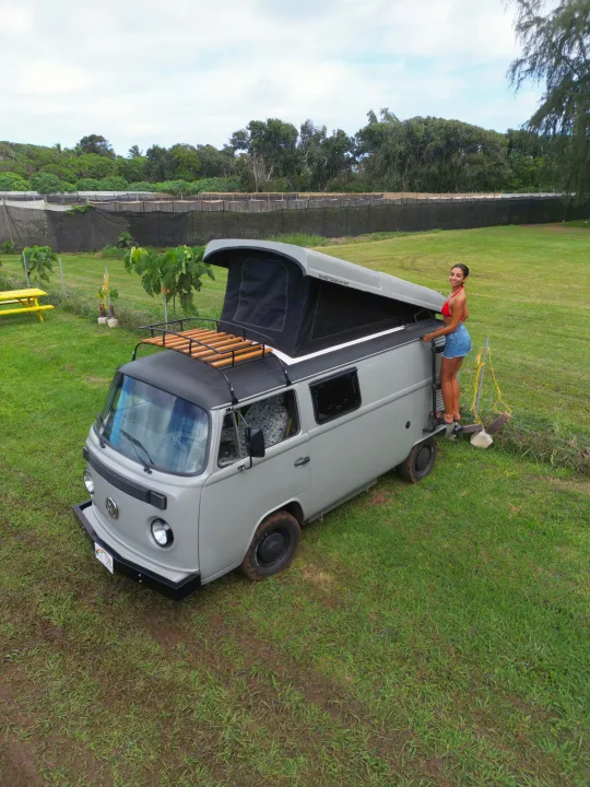 Woman with a vintage pop-top RV rental in a grassy field, ready for outdoor adventures.. Volkswagen Other 1988