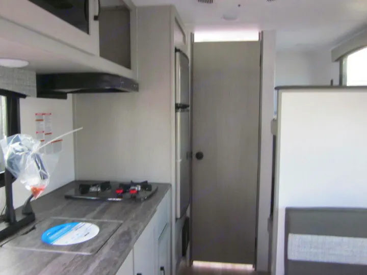 RV rental: Compact kitchen interior with stovetop, microwave, counter, and cabinets. A door is on the right.. Coachmen Clipper 2024