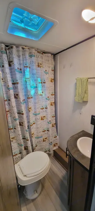 RV rental bathroom ready for camping adventures, featuring a toilet, vanity with sink, and a playful camper-print shower curtain.. Heartland RVs Pioneer 2021