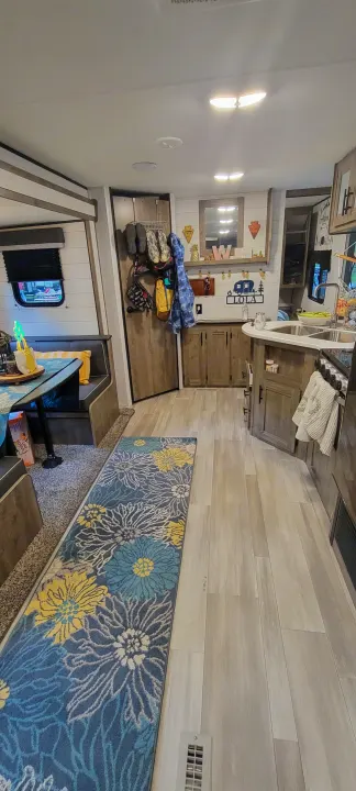 Cozy rv rental interior featuring a bright kitchen, light wood flooring, a floral runner rug, and comfortable dining booth.. Heartland RVs Pioneer 2021