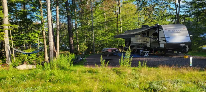 RV rental campsite: Travel trailer, picnic setup, and hammock among lush trees & grass.. Heartland RVs Pioneer 2021