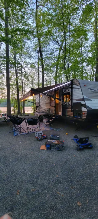 RV rental at a lakeside campsite, featuring an illuminated awning and outdoor gear for a relaxing evening.. Heartland RVs Pioneer 2021