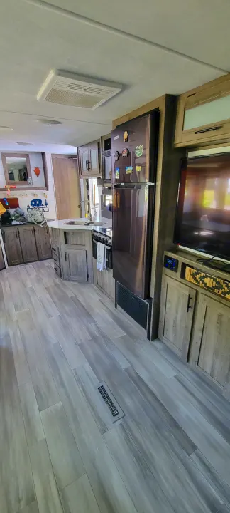 RV rental's spacious interior showcasing a modern kitchen with appliances, living area with TV, and wood-plank flooring.. Heartland RVs Pioneer 2021