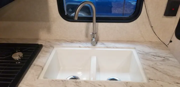 RV rental kitchen: white double-basin sink, sleek faucet, and built-in stovetop on a marble-look counter, by a window.. Jayco Jay Flight SLX 2019