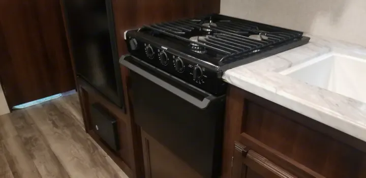 Inside an RV rental: Compact kitchen with a black Dometic stove, oven, sink, and wood cabinets.. Jayco Jay Flight SLX 2019