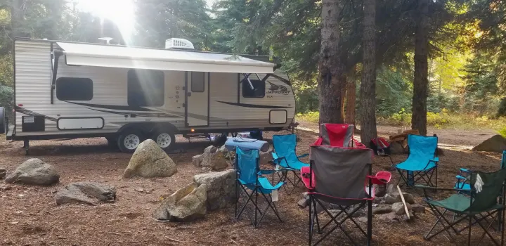 Enjoy an RV rental: a travel trailer parked in a serene, sun-dappled forest campsite with comfy chairs by a fire pit.. Jayco Jay Flight SLX 2019
