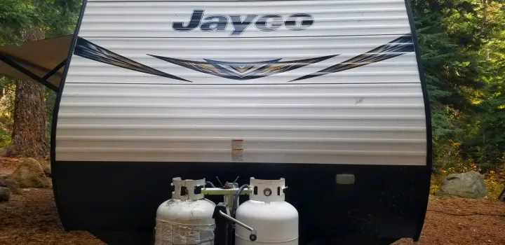 Front of a Jayco RV rental with propane tanks, parked at a peaceful campsite for outdoor travel adventures.. Jayco Jay Flight SLX 2019