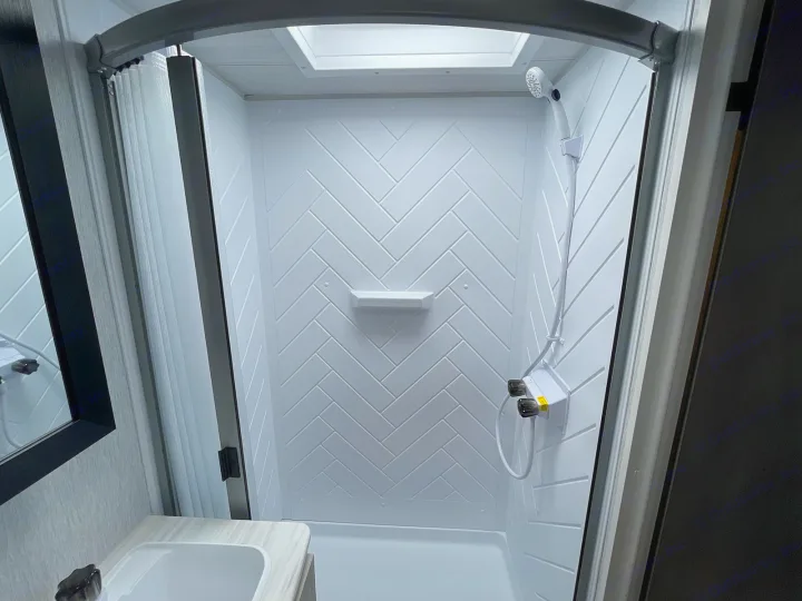 RV rental's clean, compact shower: white herringbone walls, skylight, handheld shower, and built-in shelf for toiletries.. Forest River Salem Cruise Lite 2022
