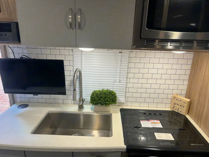 This RV rental features a modern kitchen with gray cabinets, subway tile backsplash, sink, microwave, and covered stove for efficient use of space.. Winnebago Minnie Winnie 2022