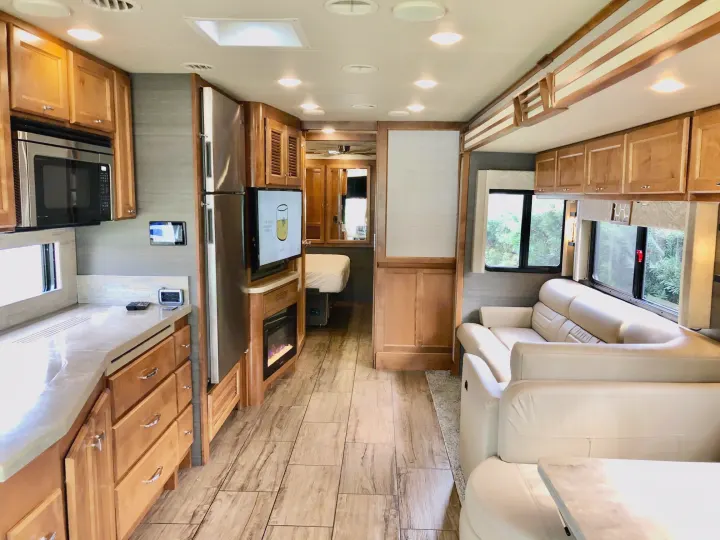 Inside an rv rental: wood kitchen cabinets, stainless appliances, comfy sofas, fireplace, and bedroom access.. Tiffin Motorhomes Allegro Open Road 2022