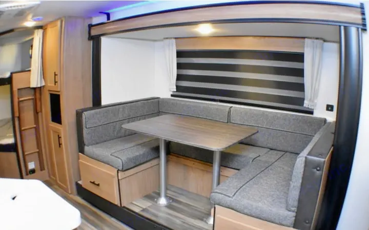 RV rental interior: cozy dinette with U-shaped seating, table, striped blinds, and bunk beds visible.. Forest River Cherokee Grey Wolf 2023