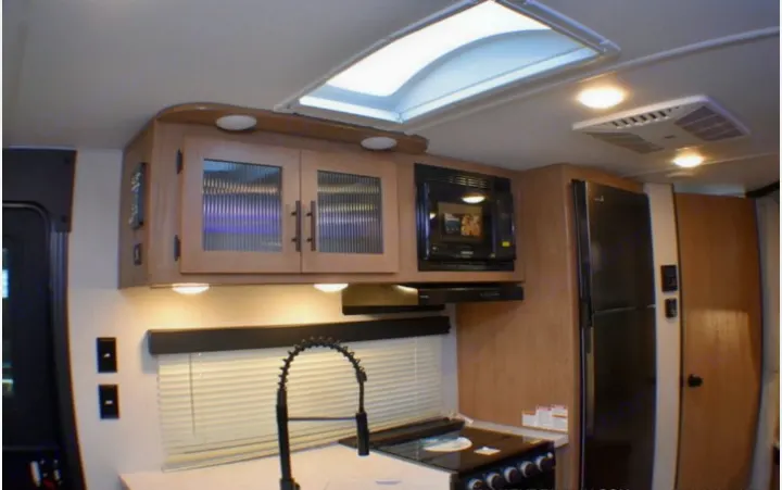 Bright RV rental kitchen with sink, stove, microwave, fridge, and cabinets. A skylight and AC ensure comfort on the road.. Forest River Cherokee Grey Wolf 2023