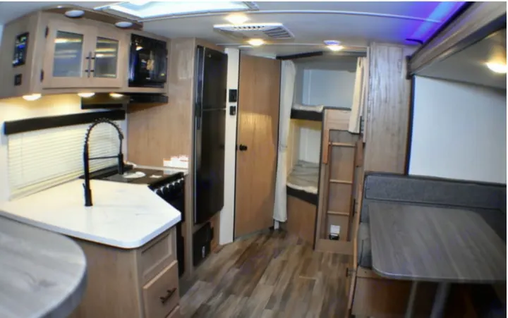 RV rental interior featuring a kitchen with stove, fridge, microwave, bunk beds, and dinette area.. Forest River Cherokee Grey Wolf 2023
