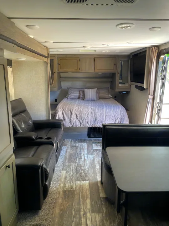 This rv rental features a cozy bedroom with a bed, comfortable recliner sofa, and a dinette booth, showcasing a spacious interior.. Keystone RV Outback Ultra-Lite 2019