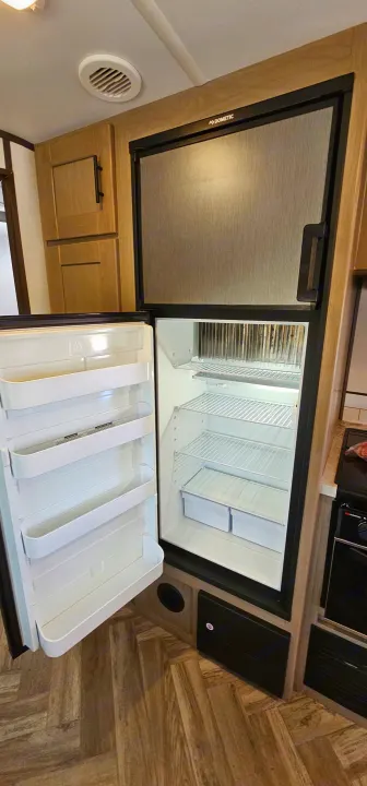 Inside an RV rental: A Dometic refrigerator with its bottom door open, showing empty shelves & crisper drawers, ready for your trip.. Cruiser RV Shadow Cruiser 2021