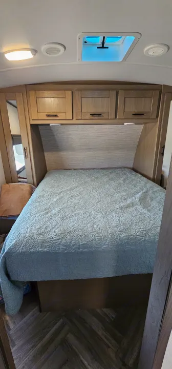 RV rental bedroom with a light blue quilted bed, wooden overhead cabinets, and a ceiling skylight, on herringbone floors.. Cruiser RV Shadow Cruiser 2021